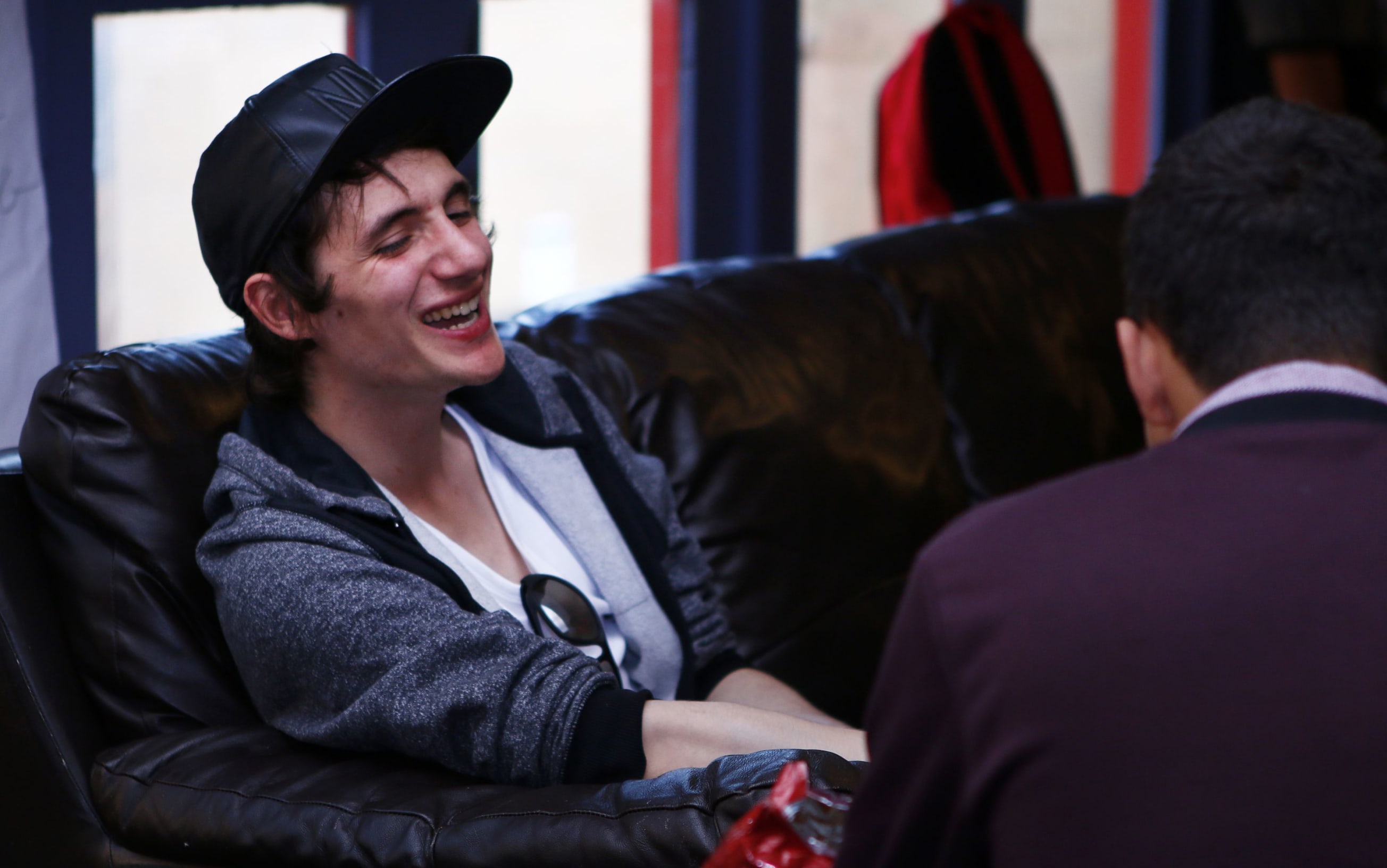 A happy young man sitting on a sofa, talking with someone facing away from the camera