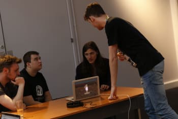 A group of young people sitting around a computer, as a staff member talks to them