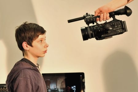An alarmed looking young man, looking into a piece of recording equipment held by someone out of frame