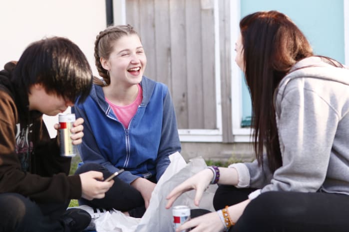 Two girls laughing with each other, with a boy looking at his phone beside them